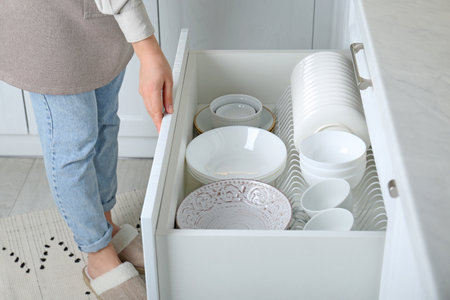 Woman opening drawer with plates and bowls in kitchen, closeupの写真素材