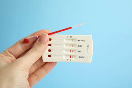 Woman holding disposable express test for hepatitis and pipette with blood on light blue background,...