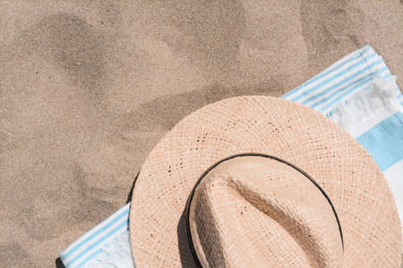 Straw hat and beach towel on sand, top view. Space for text