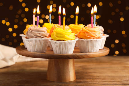 Stand with birthday cupcakes on wooden table against blurred lightsの写真素材