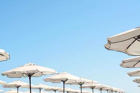 Beautiful white beach umbrellas against blue sky, space for textの写真素材
