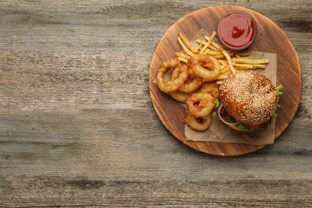 Top view of serving board with tasty burger, French fries and fried onion rings on wooden table, space for text. fast foodの写真素材