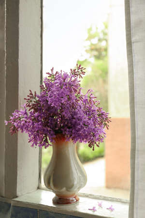 Beautiful lilac flowers in vase on window sill indoorsの写真素材