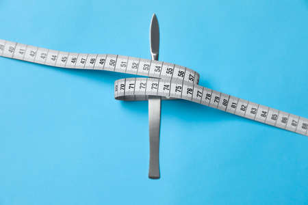 Scalpel and measuring tape on light blue background, top view. weight loss surgery
