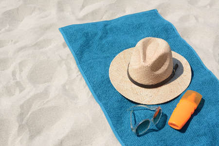 Soft blue towel, sunglasses, straw hat and bottle of sunblock on sandy beachの写真素材