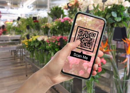 Woman holding smartphone with QR code on screen in flower shop, closeup