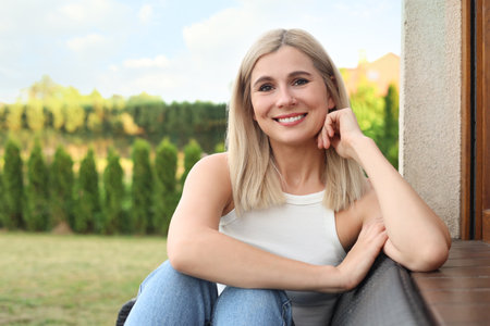 Portrait of beautiful woman sitting near house in yard, space for textの写真素材