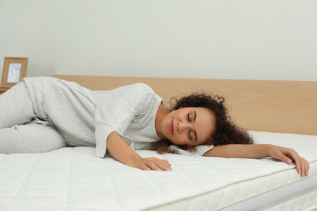 Young African American woman sleeping on bed with comfortable mattress at homeの写真素材