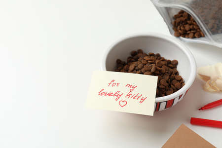 Composition with dry cat food and cute note on white table. Space for text