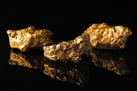 Beautiful gold nuggets on black reflective surfaceの写真素材