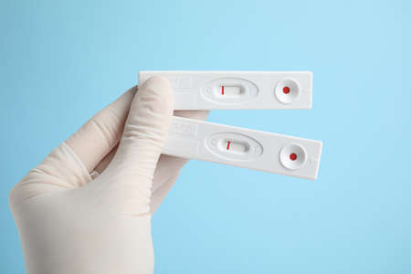Doctor holding two disposable express tests for hepatitis on light blue background, closeup