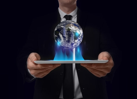 Internet technology concept. Man holding tablet and virtual icon of Earth on dark backgroundの写真素材