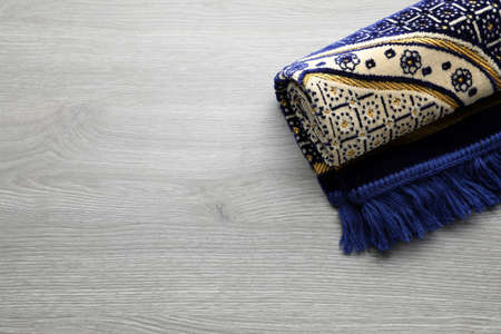 Muslim prayer rug on wooden table, top view. Space for text