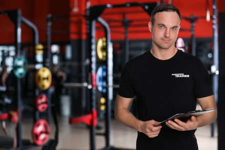 Portrait of professional personal trainer with clipboard in gym. Space for textの写真素材