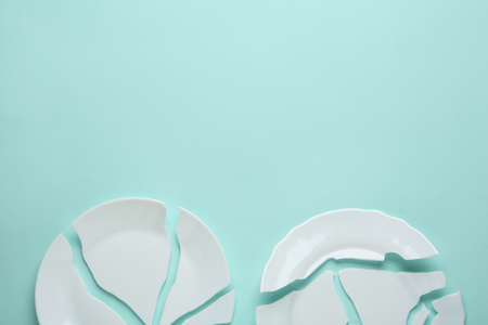 Two broken ceramic plates on light blue background, flat lay. Space for textの写真素材