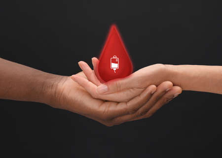 People holding red drop in hands on dark background, closeup. blood donation conceptの写真素材