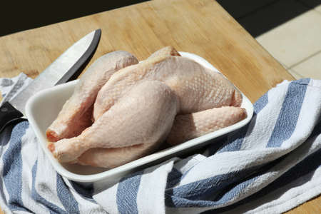 Fresh raw whole chicken in plastic container, knife and napkin on wooden table