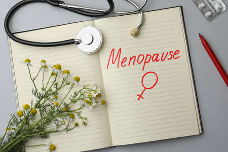 Flat lay composition of notebook with word Menopause and female gender sign on light gray backgroundの写真素材
