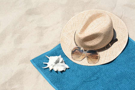 Soft blue towel, sunglasses, straw hat and seashell on sandy beachの写真素材
