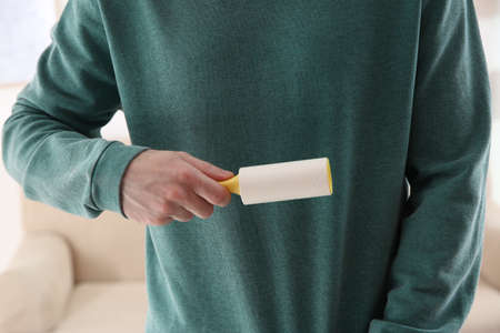 Man cleaning green sweatshirt with lint roller on light background, closeupの写真素材