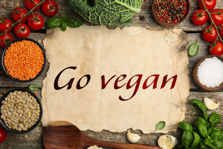 Parchment paper with phrase Go Vegan and fresh products on wooden background, flat layの写真素材