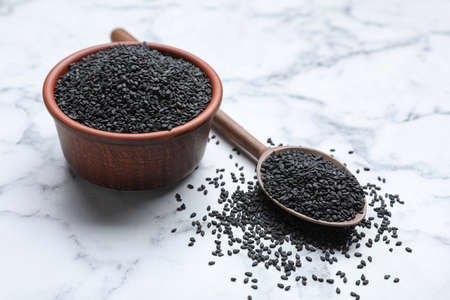 Bowl and spoon with black sesame seeds on white marble tableの写真素材