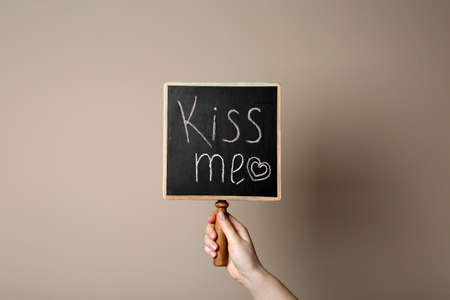 Woman holding small chalkboard with phrase Kiss Me on beige background, closeupの写真素材