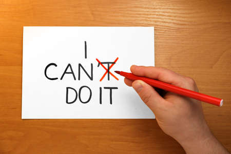 Man crossing letter T with red felt tip pen making phrase I Can Do It at wooden table, top view
