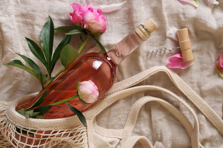 Flat lay composition with rose wine, mesh bag and beautiful peonies on white fabricの写真素材