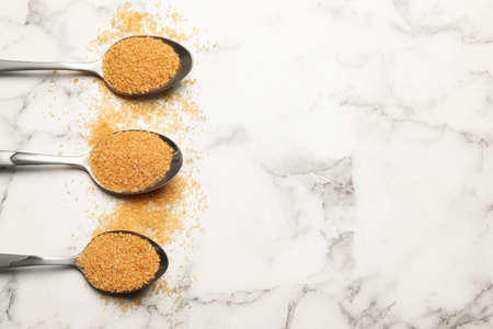 Spoons with brown sugar on white marble table, flat lay. Space for text