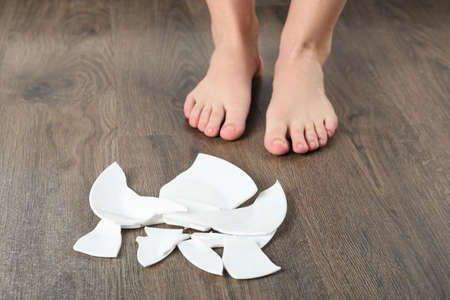 Barefoot woman standing near broken plate on floor, closeup