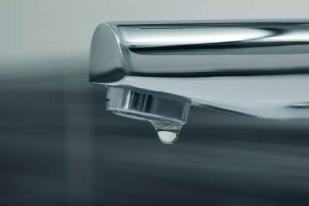Water drop falling down from tap on blurred background, closeup