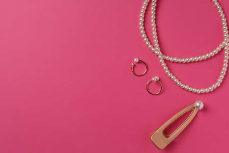 Elegant necklace, hair clips and rings with pearls on pink background, flat lay. Space for textの写真素材