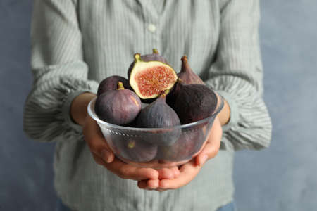 Woman holding glass bowl with tasty raw figs on light blue background, closeupの写真素材