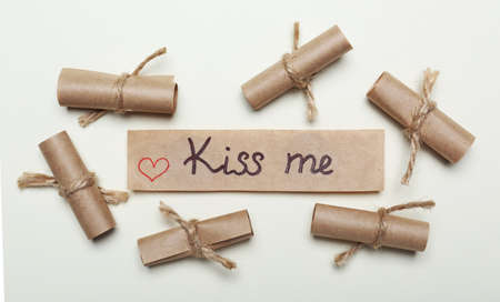 Card with phrase Kiss Me near rolled papers on beige background. flat layの写真素材