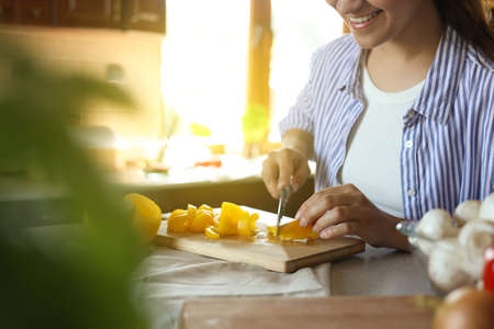 Woman cutting yellow bell peppers at countertop in kitchen, closeup. Space for textの写真素材