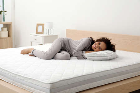 Happy young African American woman on bed with comfortable mattress and pillow at homeの写真素材