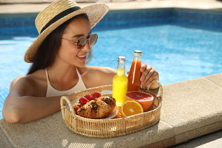 Young woman with delicious breakfast on tray in swimming poolの写真素材