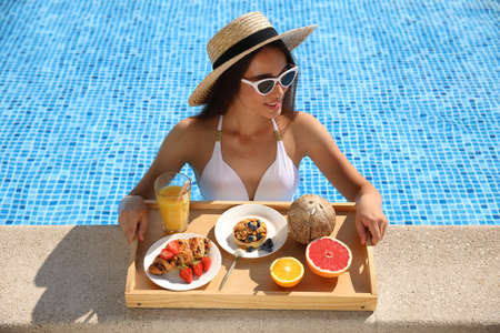 Young woman with delicious breakfast on tray in swimming poolの写真素材