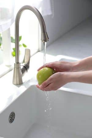 Woman washing apple over sink in kitchen, closeupの写真素材