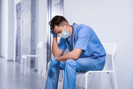 Exhausted doctor sitting on chair in hospital hallwayの写真素材