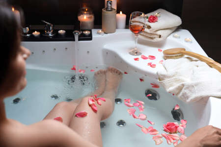 Woman taking bath with rose petals, closeup. romantic atmosphere