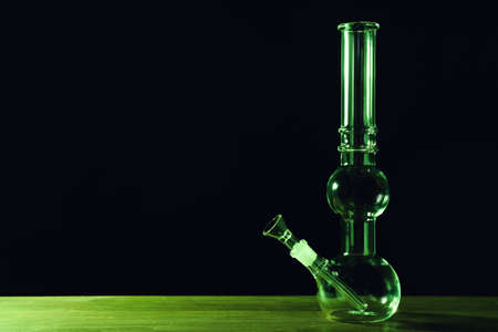 Glass bong on wooden table against black background, space for text. smoking device