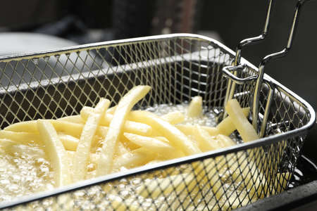 Cooking delicious french fries in hot oil, closeupの写真素材