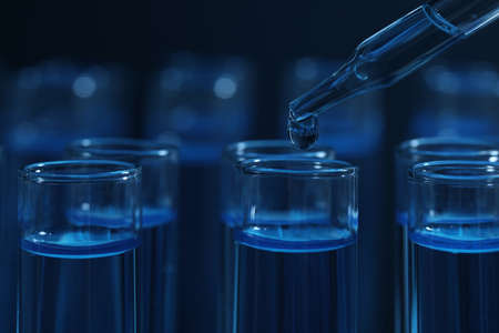 Dripping reagent into test tube with blue liquid on dark background, closeup. laboratory analysis