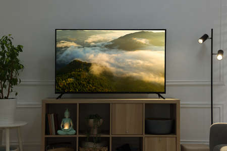 Modern TV set on wooden stand in room. Scene of nature themed movie on screen