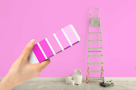 Decorator holding color palette samples in room with painted wall, closeup. interior renovation