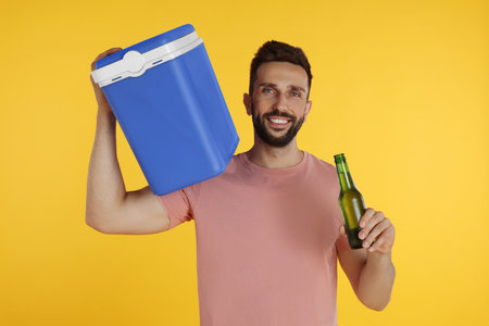 Happy man with cool box and bottle of beer on yellow backgroundの写真素材