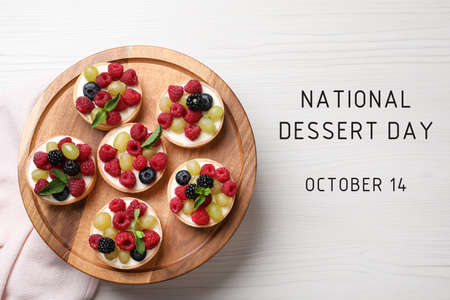 National Dessert Day, October 14. Delicious tartlets with fresh berries on white wooden table, top...