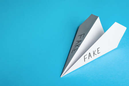 Paper plane with words FAKE on light blue background, top view. Space for textの写真素材